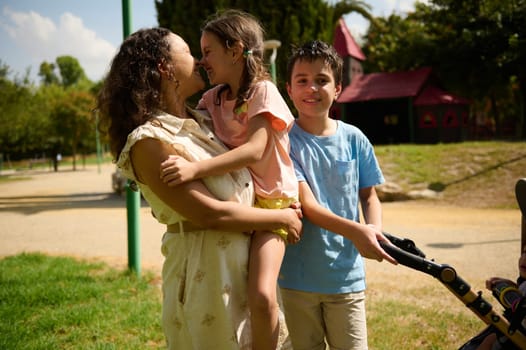 A joyful family spends a cheerful day at the park, enjoying nature and togetherness. The mother holds her daughter, while the son stands beside them, smiling.
