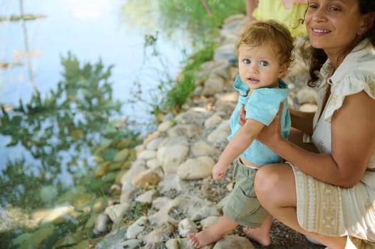 A smiling mother and child enjoy a sunny day by a peaceful pond, reflecting happiness.