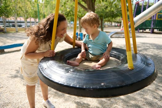 A mother and child playing on a tire swing in a sunny playground setting, sharing laughter and joy during a delightful day outdoors.