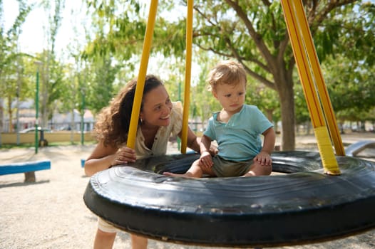 Loving mother and child delight in a sunny day at the park, playing on a swing. Capturing joyful moments and bonding during leisure time outdoors.