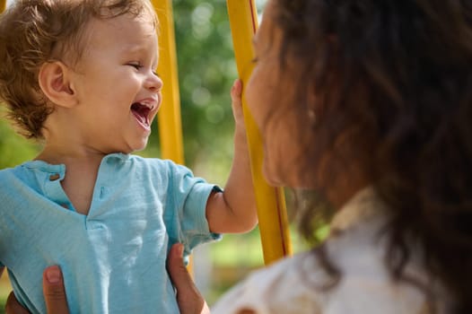 A mother and child share a happy moment outdoors, capturing joyful expressions and love. The child is laughing affectionately, embraced by the mother in a bright, sunny park.