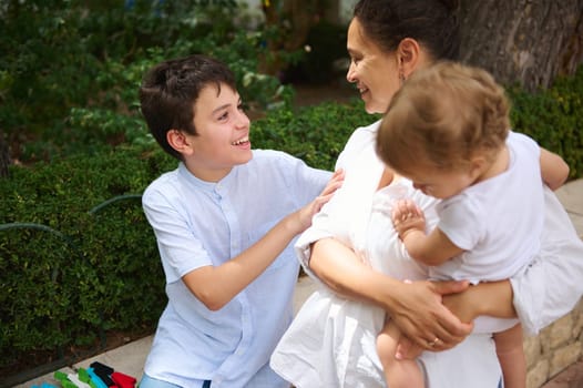 A joyful mother interacts with her children outside, fostering a loving family bond. The scene captures a sunny day filled with laughter and warmth in a garden environment.