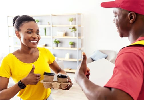 Courier Service. African American Delivery Guy And Happy Female Customer Gesturing Thumbs Up Standing In Doors Of Home. Cheerful Black Lady Receiving Coffee And Food From Restaurant