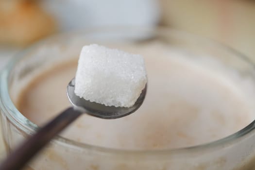 A hand delicately holding a sugar cube high above a steaming cup of rich coffee