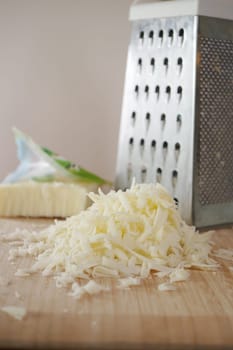 Freshly grated cheese beautifully piled next to a metal grater resting on a wooden surface