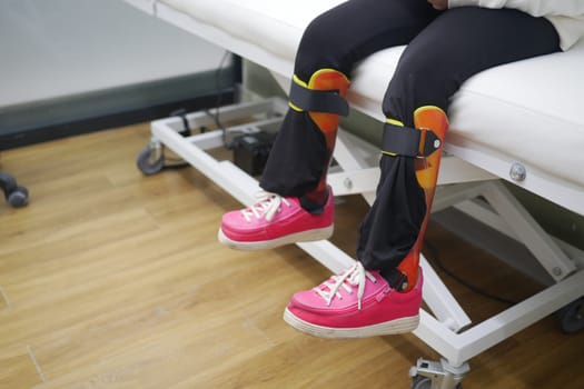 Child's Legs With Orthopedic Braces and Bright Pink Shoes on Clinic Bed.