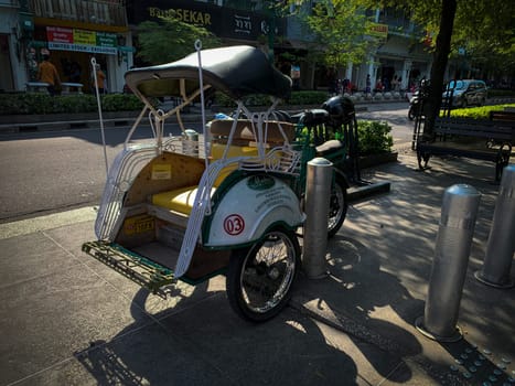 pedicab or rickshaw or locals calls it becak with a canopy is parked on a sunny street, reflecting a vibrant urban scene. The vehicle features a padded seat and unique design
