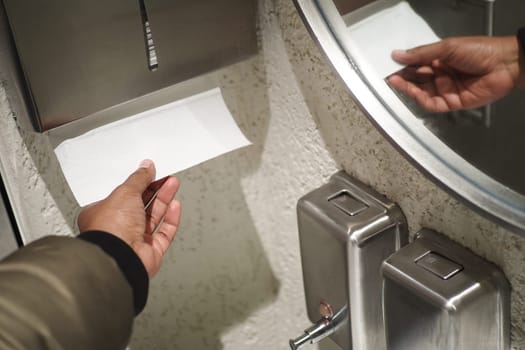 Hand taking paper towel from a dispenser in a clean public restroom with white tiles.