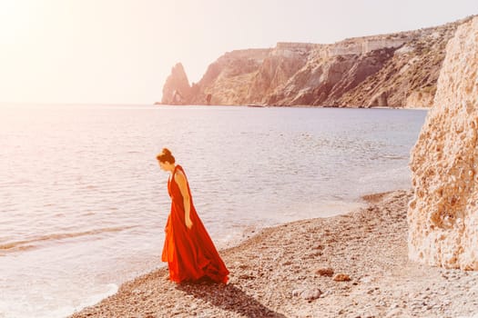 Woman red dress sea. Female dancer in a long red dress posing on a beach with rocks on sunny day. Girl on the nature on blue sky background
