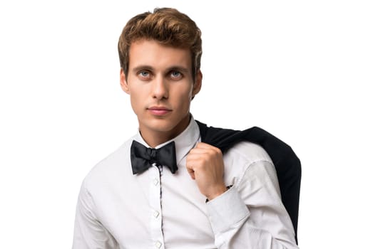 Elegant young man in white shirt standing holding coat over shoulder and looking at camera on white background