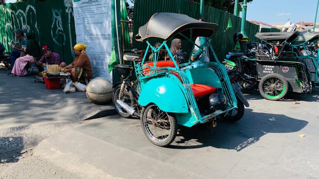 pedicab or rickshaw or locals calls it becak with a canopy is parked on a sunny street, reflecting a vibrant urban scene. The vehicle features a padded seat and unique design