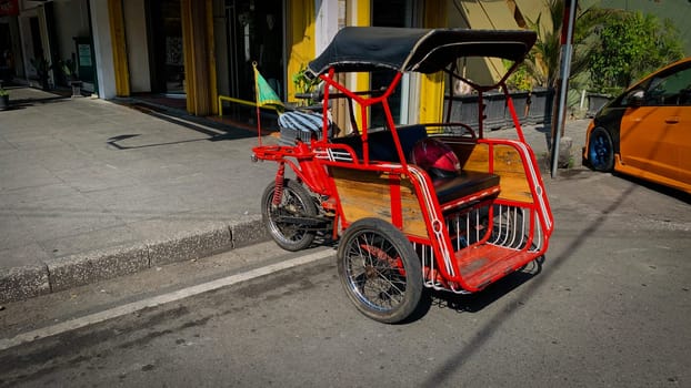 pedicab or rickshaw or locals calls it becak with a canopy is parked on a sunny street, reflecting a vibrant urban scene. The vehicle features a padded seat and unique design