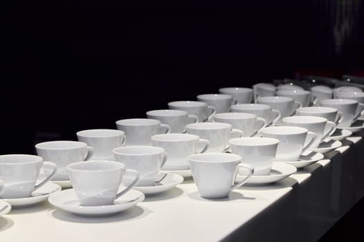 An elegant array of pristine white coffee cups and saucers displayed on a sleek table, perfect for any occasion