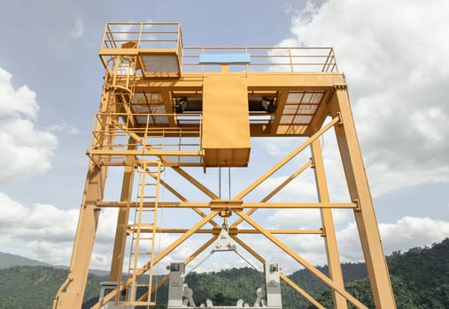 Nakhon Nayok, Thailand - 07 Dec, 2024 - View of Yellow gantry overhead crane control watergate and water in the dam between the hills at The Khun Dan Prakan Chon Dam, Nakhon Nayok Province, Thailand, Crane overhead beam machine with sky and clouds in the background, use it as your Copy space, Selective focus.