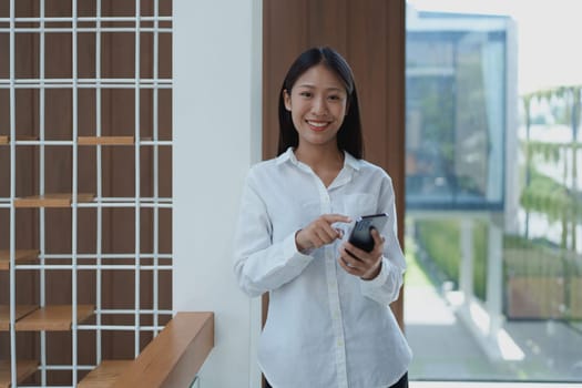 A young woman in a stylish office smiles while using her smartphone. The image highlights modern workspace and technology in professional life with natural lighting.