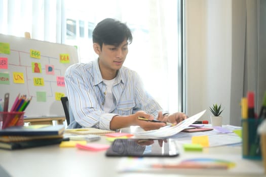 UX designer reviewing mobile application wireframes and color palettes at office desk.