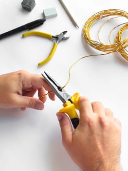 Hands using pliers to trim wire with tools on white surface for diy project.
