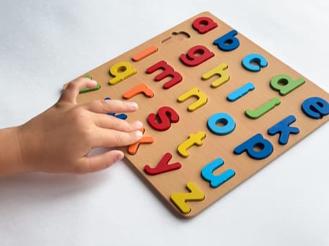 Child learning with colorful alphabet puzzle on white background.