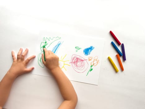 Child drawing colorful art with crayons on paper.