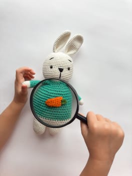 Child exploring amigurumi rabbit with magnifying glass and carrot design.