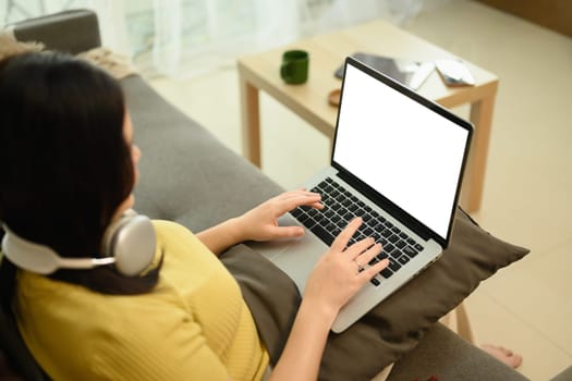 Overhead view of young woman typing on a laptop while sitting on couch.