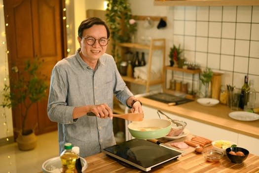Joyful smiling middle aged man preparing a meal in a cozy kitchen..