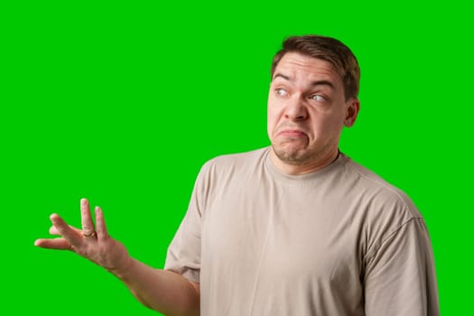 A man stands with arms crossed and a thoughtful expression in front of a green screen in studio