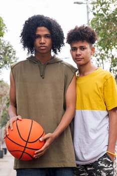 two serious african american teens standing close with basketball in park and looking at camera, concept of youth and urban lifestyle