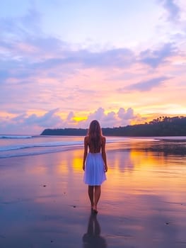Woman inA tranquil scene of a woman in a flowing white dress walking barefoot along a beach during sunset. The vibrant sky reflects on the wet sand, creating a peaceful and dreamlike atmosphere.