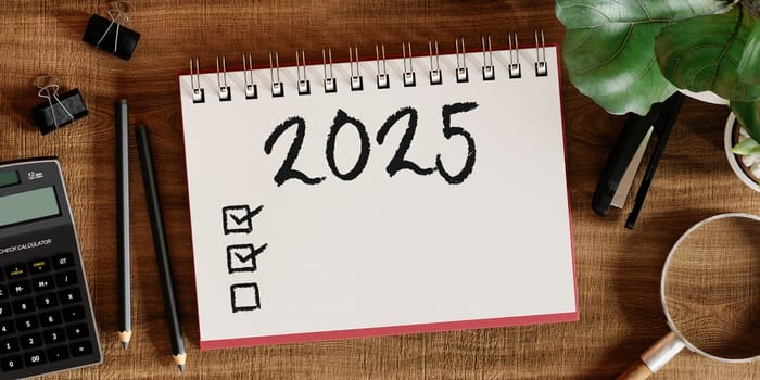 2025 checklist notebook with a calculator and other office supplies on a tidy desk, ideal for organized task management.