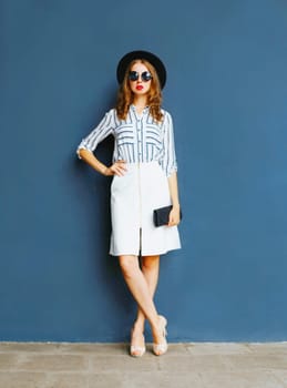 full length fashion elegant woman in a black hat, white skirt with a handbag clutch over a gray background