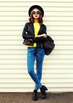 Fashionable stylish young woman full length posing in black jacket with backpack on white background