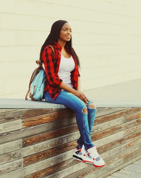 Fashion smiling african woman wearing a red checkered shirt and backpack resting in the city park