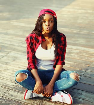 Fashion young african woman is having fun in the city, wearing red checkered shirt and baseball cap