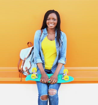Portrait of happy smiling young african woman model posing with skateboard in the city