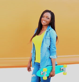 Portrait of happy smiling young african woman model posing with skateboard in the city