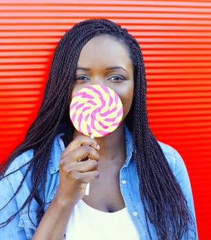 Portrait happy smiling african woman with sweet lollipop over red background