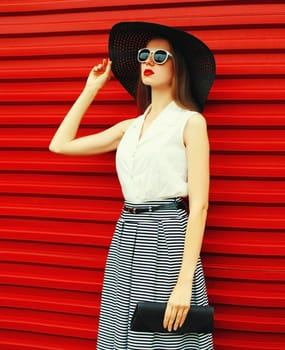 Portrait of stylish young woman model posing wearing summer round hat, handbag on red background