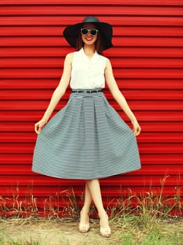 Portrait of stylish young woman model posing wearing black summer straw round hat on red background