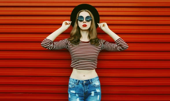 Portrait of stylish young woman posing wearing a black round hat on a red background