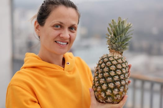 A cheerful and joyful woman proudly showcasing a fresh and ripe pineapple against a vibrant city backdrop