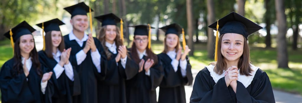Group of happy students in graduation gowns outdoors. A young girl in the foreground