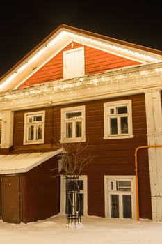 A wooden house decorated with Christmas glowing garlands at night. Festive decorations in the city, garlands and lights.