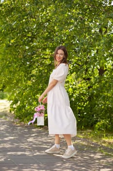 Beautiful girl with flowers, in a dress, glasses and sneakers. A beautiful bouquet of flowers in a box in the hands of a beautiful girl who walks along the street on a sunny day.