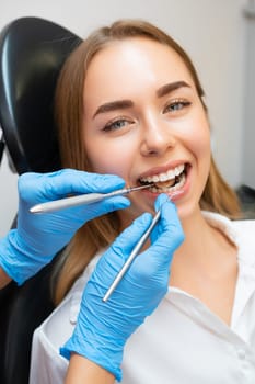 Close-up woman patient sitting in armchair during dental treatment in dental clinic. Doctor checking front teeth with instrument to check soundness of teeth