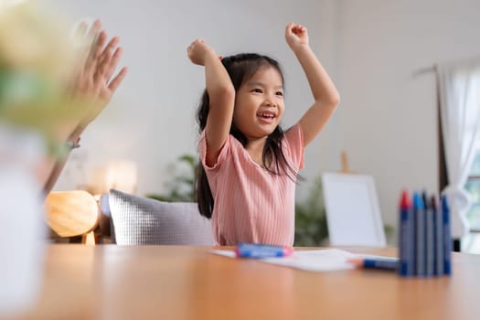 A little girl is happy to finish a draw with her mother in the living room at home. Excited mother give high five to small daughter praise child for reaching success.