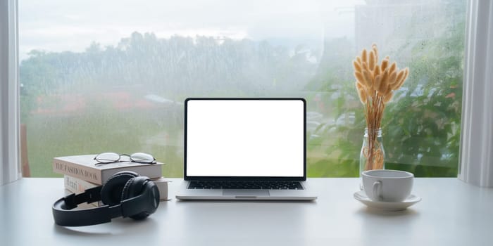 Image of working space by the window equipment in office interior, open laptop computer with mock up screen.