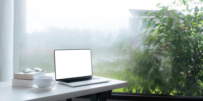 Image of working space by the window equipment in office interior, open laptop computer with mock up screen.