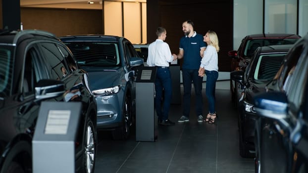 A caucasian couple shakes hands with a salesperson while buying a car