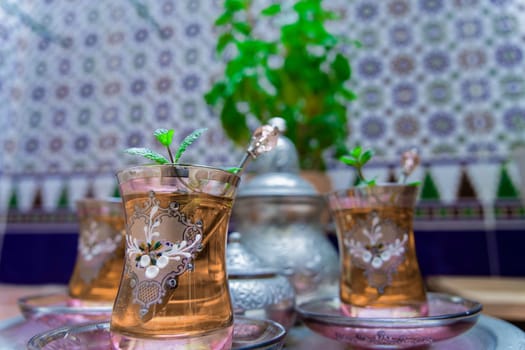 Moorish tea with mint, traditional Moroccan drink in decorated crystal glasses, silver teapot and sugar bowl in the background.